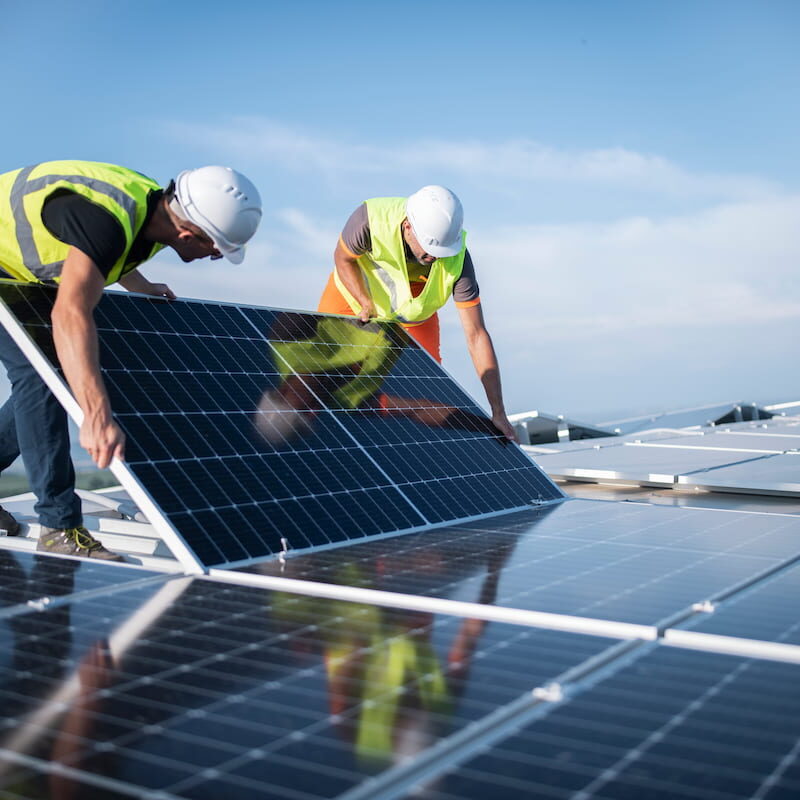 Two men in high vis gear placing a solar panel