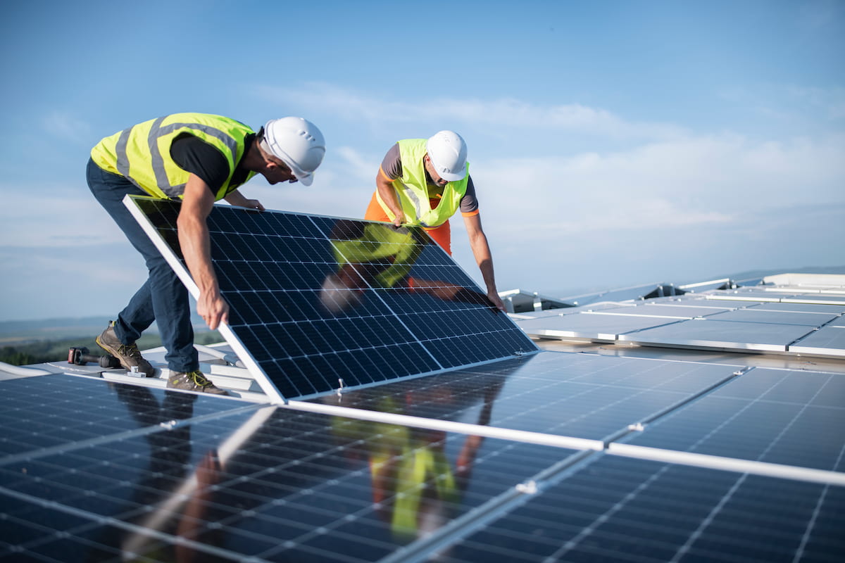 Two men in high vis gear placing a solar panel