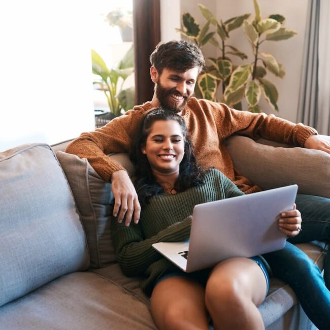 A couple reclining on a sofa with a laptop