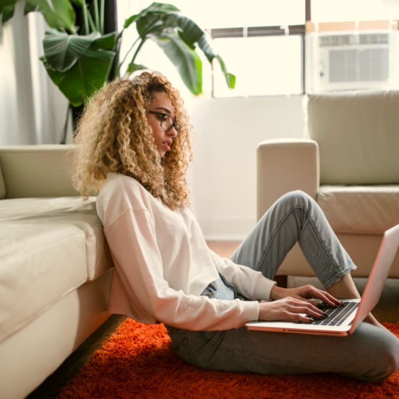 Woman sat on the floor of a modern home with a laptop