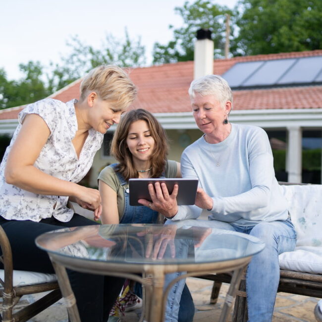 Three generations of women in a garden looking at a tablet, with a solar array visible behind them