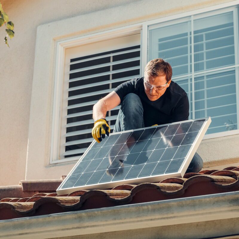 A middle aged white man placing a single solar panel on a roof